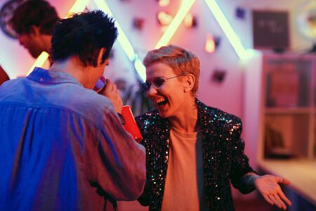 Young couple laughing and drinking beer from glasses while having fun at the party