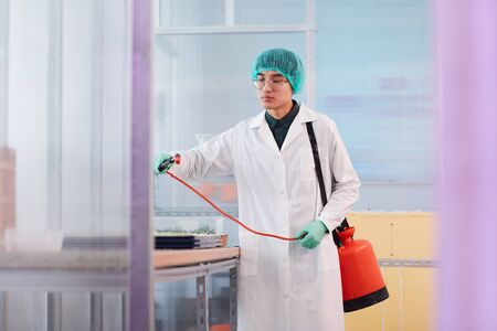 Asian young chemist in white coat standing near the table and processing seeds with chemicals in the...