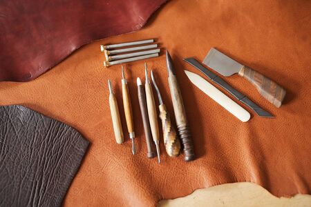 Horizontal high angle shot of various craftwork tools and pieces of leather material of different...