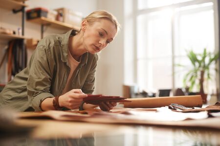 Horizontal portrait of young adult female artisan attentively choosing material for her new...