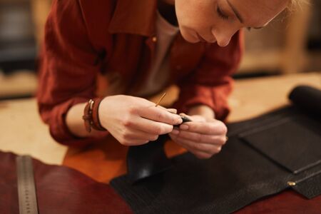 Horizontal shot of young female artisan creating something using leather materials of different coloursの写真素材