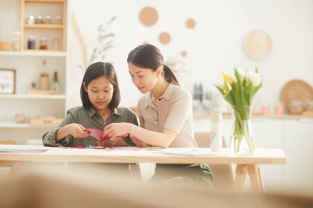 Two sisters sitting together at table in kitchen room cutting out cardboard hearts for Mothers Day cardsの写真素材