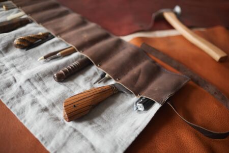 Horizontal high angle shot of various tools in handmade case, claw hammer and pieces of leather material on tableの写真素材