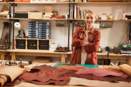 Horizontal shot of cheerful young Caucasian woman standing in her workshop with arms crossed looking at camera smilingの写真素材