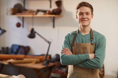 Horizontal medium portrait of young Caucasian craftsman wearing apron standing with arms crossed looking at camera smilingの写真素材