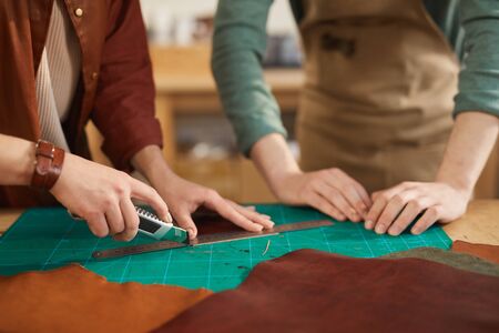 Hands of unrecognizable man and woman working together in modern leather craft workshop, copy space
