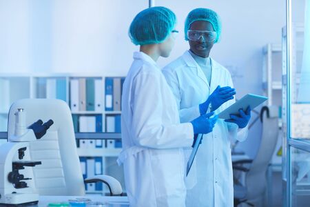 Horizontal medium long shot of two young man and woman working in laboratory together discussing...