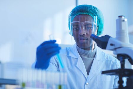 Horizontal chest up portrait of young male medical scientist wearing protective mask doing...