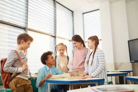 Group of five happy friends chatting about something funny during break time at school, copy space