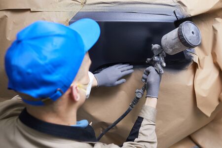 Horizontal close up high angle back view shot of unrecognizable man in uniform painting car body...