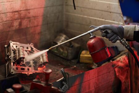 Unrecognizable man sandblasting car motor part to clean it, horizontal shot, copy space