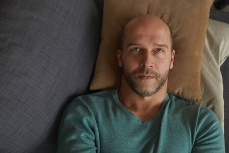 High angle view of mature man lying on the sofa on pillow and dreaming about somethingの写真素材