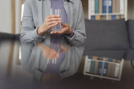 Close-up of young woman holding glass of water in her hands while sitting at office