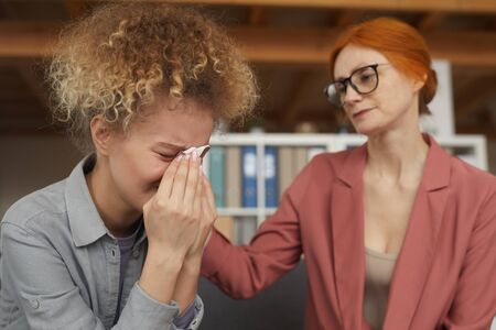 Young woman with curly hair sitting and crying with her friend supporting her in difficult situationの写真素材