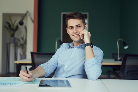 Young businessman has a consultation on mobile phone and working with documents at his workplace at...