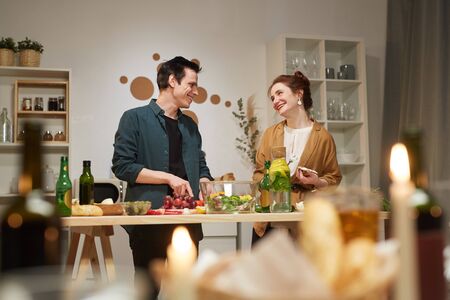 Young couple smiling to each other while cooking dinner together in domestic kitchen