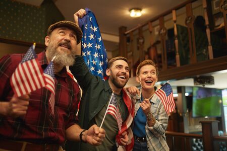 Group of friends with American flags watching football match in sport barの写真素材