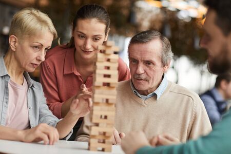 Group of friends playing in wooden block together they sitting at the table and concentrating on the gameの写真素材