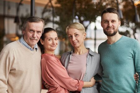 Portrait of family of four embracing each other and smiling at camera while standing at the...
