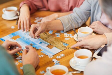 Close-up of family of four sitting at the table drinking tea and collecting puzzles togetherの写真素材