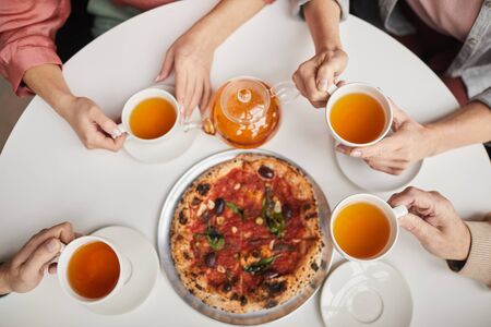 High angle view of family sitting at the table with cups of tea and eating pizzaの写真素材