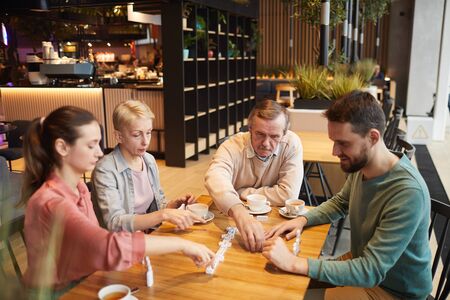Group of people sitting at the table and playing in domino while drinking tea in cafe