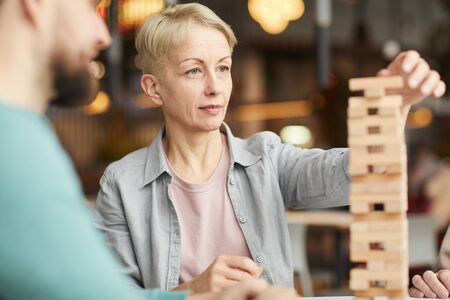 Mature woman playing with wooden details together with her friends at the table