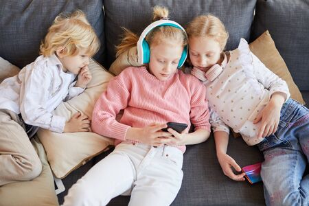 Group of children lying on sofa and using mobile phone to play in online game at home
