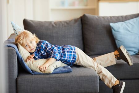Portrait of little boy in casual clothing lying on sofa and resting in the living room at homeの写真素材
