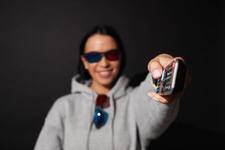 Portrait of young woman switching on the TV and watching movie in 3D glasses over black backgroundの写真素材