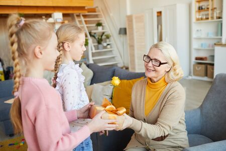 Happy grandmother in eyeglasses getting present from her grandchildren while they are in the living...