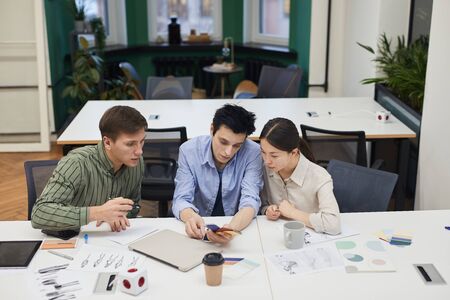 Group of creative designers examining colored patterns and working over new fashion collection at...