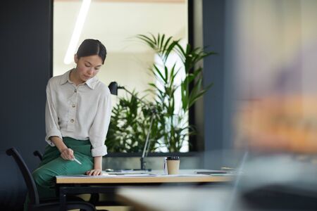 Asian young businesswoman sitting at the table and reading documents she preparing for the meeting...