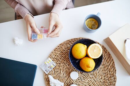 Close-up of woman sitting at the table and taking out the pills from the box and she drinking course at homeの写真素材