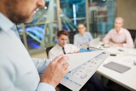 Close-up of businessman holding report in his hands and examining it before the business...