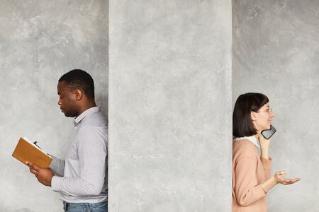 African businessman reading his note pad with businesswoman talking on the mobile phone they standing back to back behind the white wallの写真素材