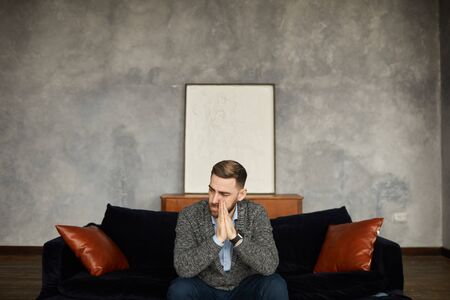 Disappointed young businessman sitting on sofa with pensive look and looking awayの写真素材