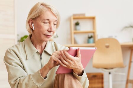 Mature serious woman using digital tablet at home she typing on the digital screen and listening to...