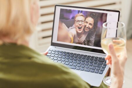 Two happy women on computer monitor talking online with their friend who sitting at homeの写真素材