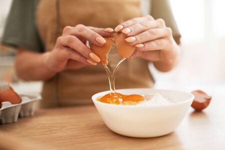 Close-up of young woman breaking eggs in a bowl while standing at the table she making a doughの写真素材