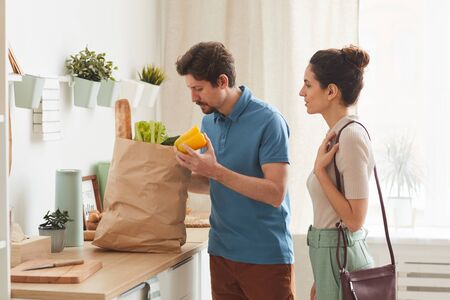 Young couple buying fresh vegetables in paper bag they bringing them to home in the kitchenの写真素材