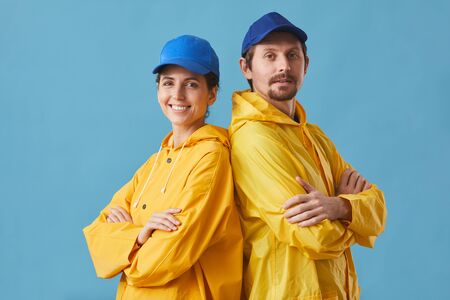 Portrait of young couple in uniform working in delivery service standing with arms crossed and smiling at camera against the blue backgroundの写真素材