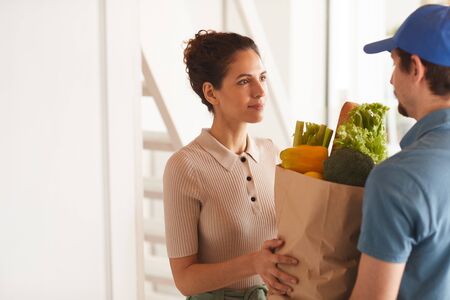 Young woman getting products from delivery man she ordering food at homeの写真素材