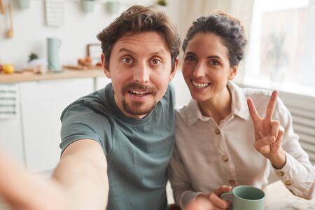 Portrait of happy young couple making selfie portrait during breakfast at homeの写真素材