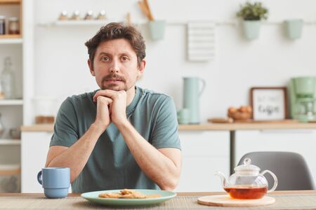 Portrait of young man sitting at the table and looking at camera during his breakfast at homeの写真素材