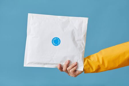 Close-up of female hand holding parcel packed in white paper isolated on blue backgroundの写真素材