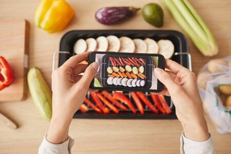 High angle view of woman holding mobile phone and photographing her prepared dish from vegetablesの写真素材