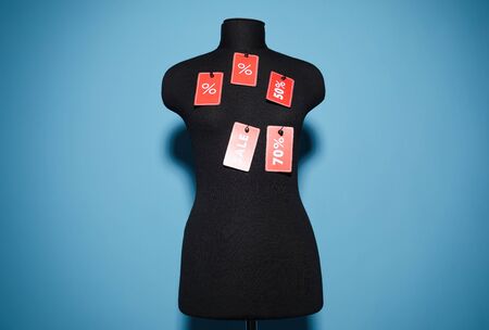 Image of black mannequin with sale and discount signs on it isolated on blue backgroundの写真素材