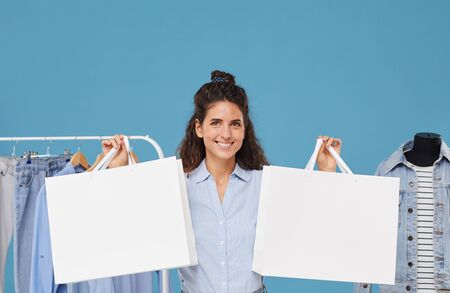 Portrait of young happy woman buying clothes she holding shopping bags in her hands isolated on blue...