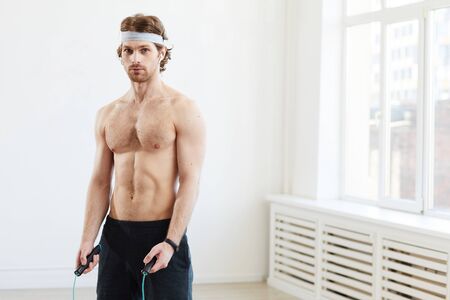 Portrait of young muscular man looking at camera while training with skipping rope